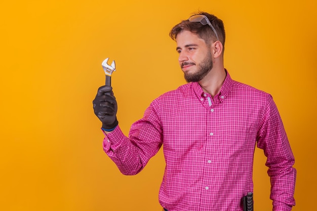Positive and confident repairman with tool kit on his hip and screwdriver smiling and looking at camera, against white background.