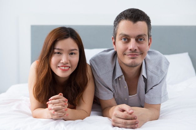 Positive couple lying on soft duvet in bedroom