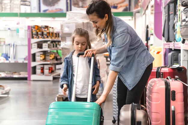 Позитивные пары с ребенком, покупая чемодан на колесах для отдыха в магазине