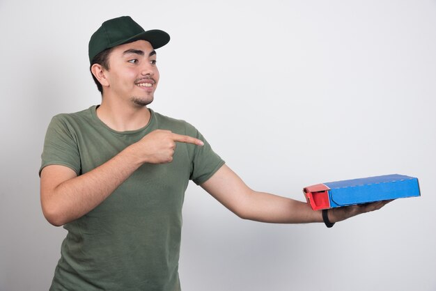 Positive courier pointing at pizza and showing thumbs up on white background.