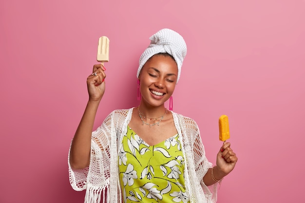 Positive dark skinned woman smiles broadly holds delicious ice cream keeps eyes closed