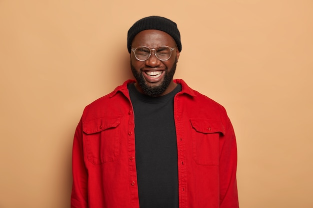 Free photo positive dark skinned young man has thick bristle, smiles broadly with white perfect teeth