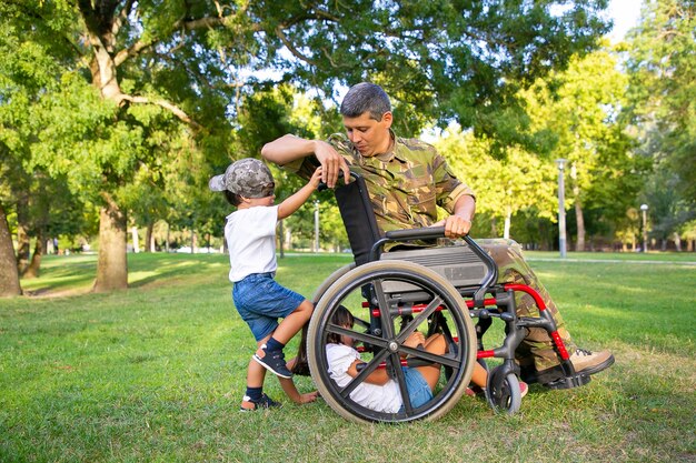 공원에서 아이들과 함께 시간을 즐기고 긍정적 인 장애인 군사 아빠. 잔디에 휠체어를 가지고 노는 아이들. 참전 용사 또는 장애 개념