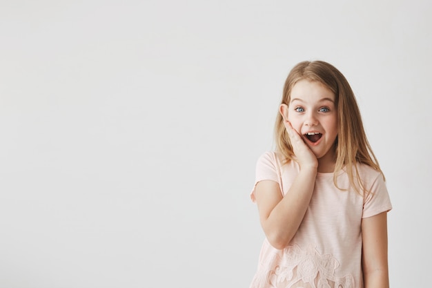 Positive emotions and expressions. Cute little girl  with happy and excited expression, holding hand on cheek, being surprised to get flowers from boy.