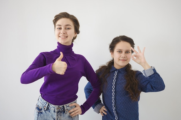 Positive emotions, signs and gestures concept. Two beautiful cheerful Caucasian sisters recommending you something