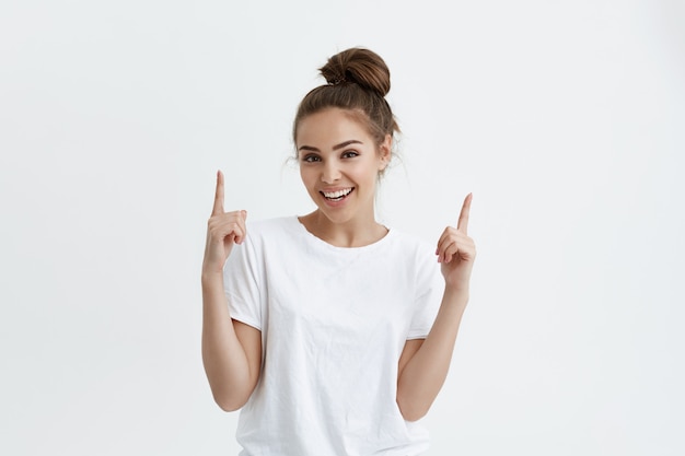 Positive european woman pointing up with both index fingers while smiling cheerfully