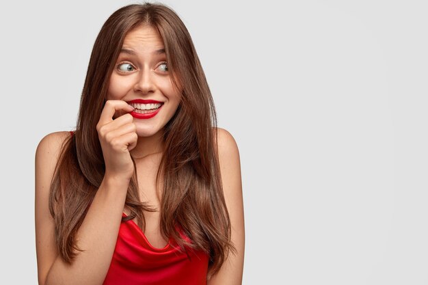 Positive European woman with mysterious happy expression, keeps index finger near mouth