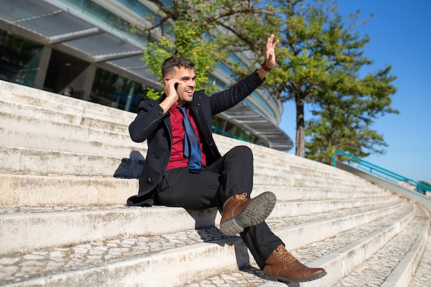 Positive excited businessman waving hand while talking on phone