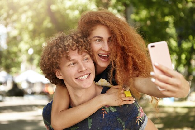 Positive female hugging her boyfriend and holding cell phone