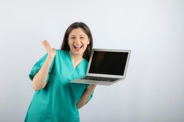Положительная медсестра позирует с ноутбуком на белом.