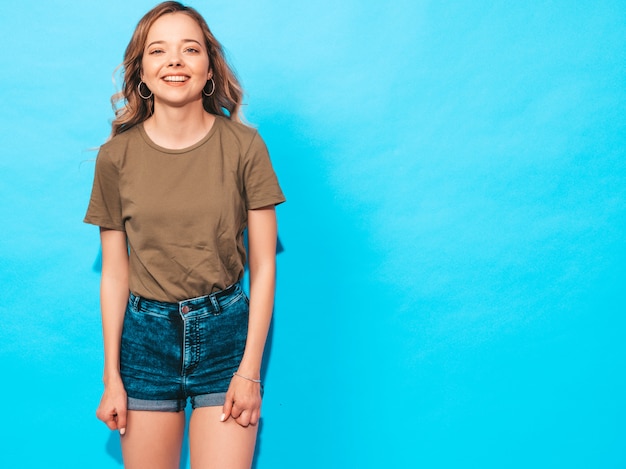 Sorridere femminile positivo modello divertente che posa vicino alla parete blu in studio