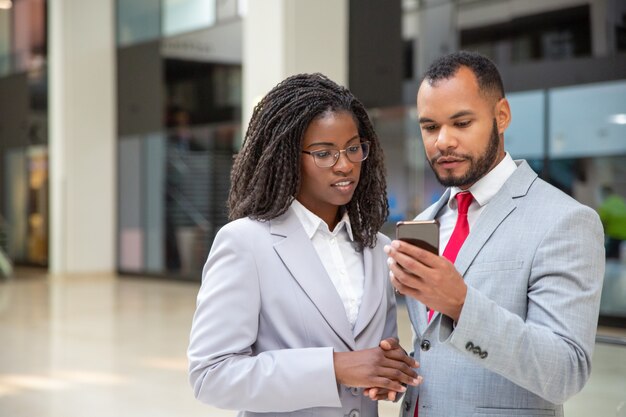 Positive focused colleagues looking at mobile phone screen