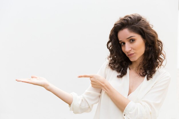 Positive friendly woman pointing finger and holding copy space