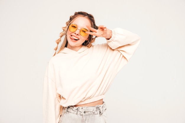 Positive and funny model posing on grey wall in studio in sunglasses