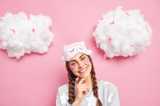 Free photo positive gentle caucasian female model has two pigtails smiles broadly tilts head wears blindfold and pajama