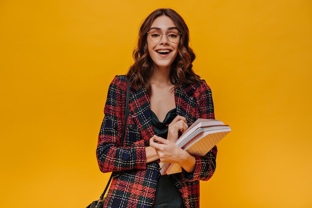 Positive girl in glasses and striped jacket smiling on yellow wall