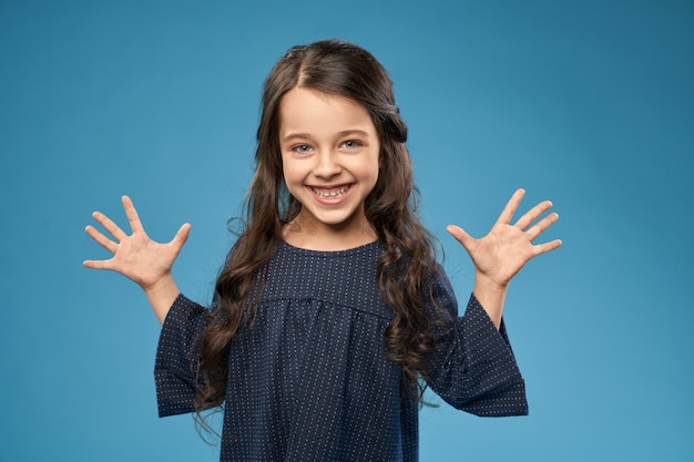 Ragazza positiva in vestito grigio che mostra le dita, mani.