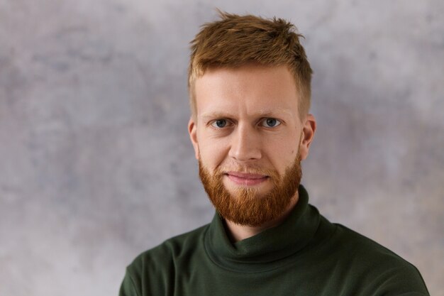 Positive good looking handsome man wearing dark green turtleneck sweatshirt having cheerful confident facial expression. Isolated shot of charismatic easy going young man with beard smiling