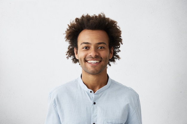 Foto gratuita ragazzo positivo con acconciatura africana e pelle scura che indossa un'elegante camicia bianca