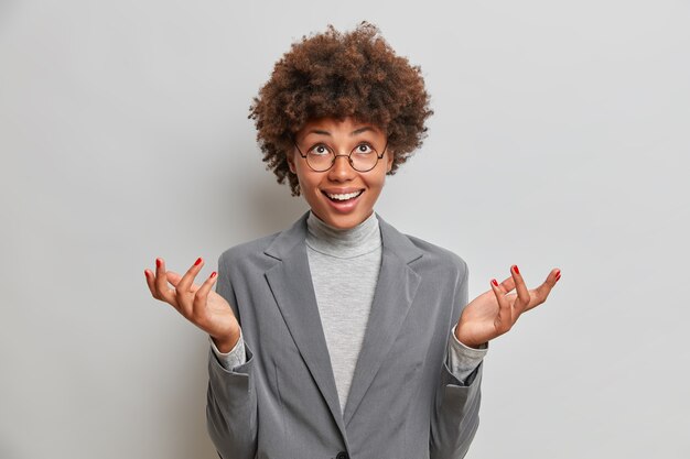 Positive hesitant business lady speads palms clueless, looks up at ceiling, hesitates over choice, dressed formally