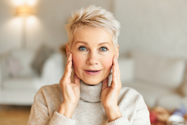Positive human facial expressions, feelings, emotions and reaction. Picture of emotional attractive mature female with blonde hair and blue eyes holding hands on face, being amazed with something
