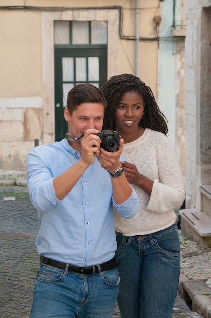 通りでカメラに写真を撮る肯定的な異人種間のカップル