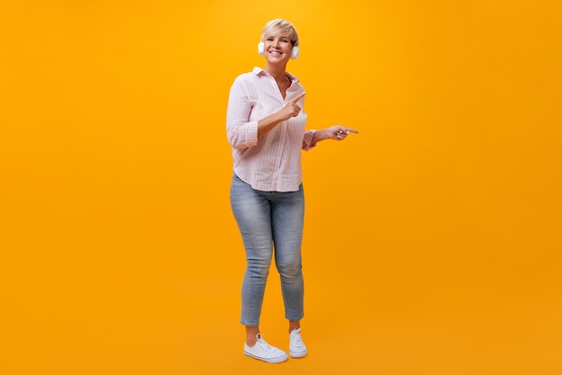 Бесплатное фото Позитивная дама в джинсах и рубашке танцует и слушает музыку в наушниках