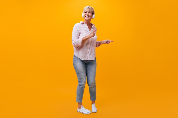 Positive Lady in jeans and shirt dancing and listening to music in headphones