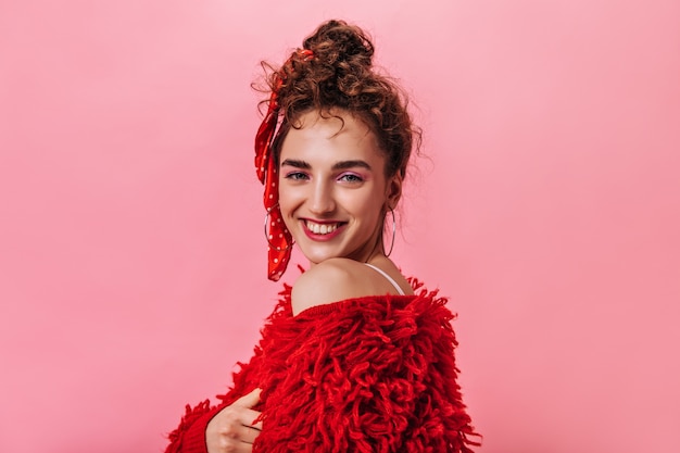 Positive lady in red outfit smiling and looking into camera on pink