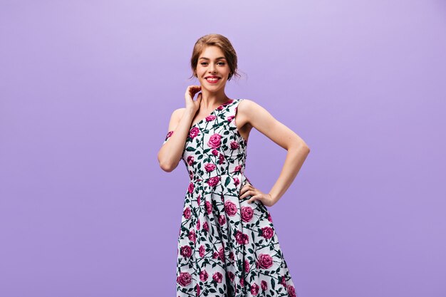 Позитивная дама в модном платье улыбается на фиолетовом фоне. Замечательная волнистая женщина в стильной цветочной одежде позирует в камеру.