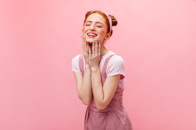 Positive lady with gentle make-up dressed in pink dress laughs on isolated background.