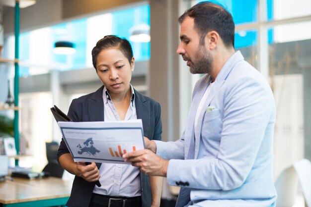 Positive Latin man showing report to Asian woman with folder