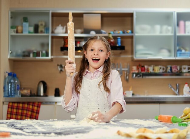 Позитивная маленькая девочка-подросток делает тесто на домашней кухне.