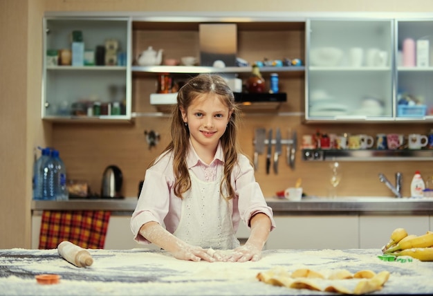 Positive little teenage girl making dough in the home kitchen.