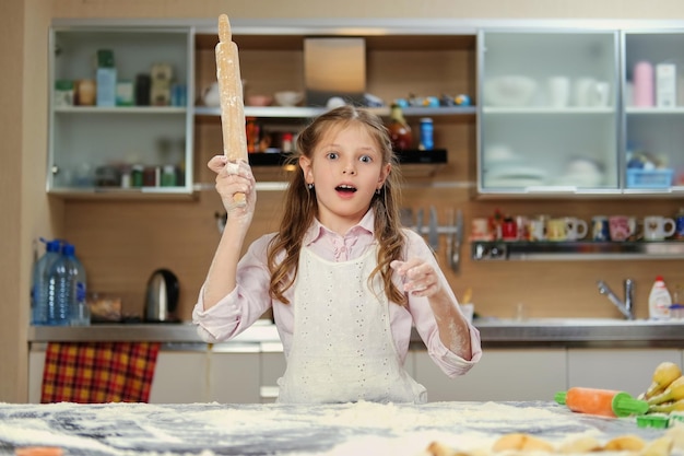 Позитивная маленькая девочка-подросток делает тесто на домашней кухне.