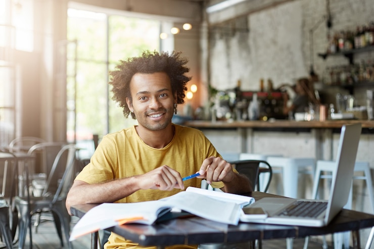 Free Photo positive male sitting at desk at coffee shop using laptop