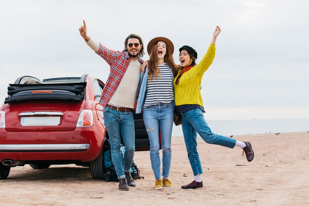 Positive man and crying women embracing near car on sea coast