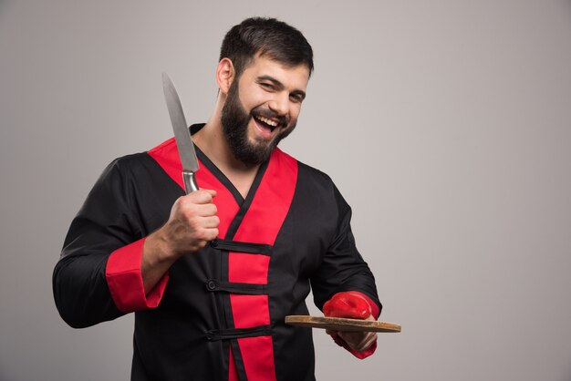 Positive man holding wooden board with red pepper and knife.