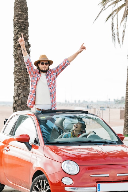 Free photo positive man with upped hands leaning out from car and smiling woman in auto