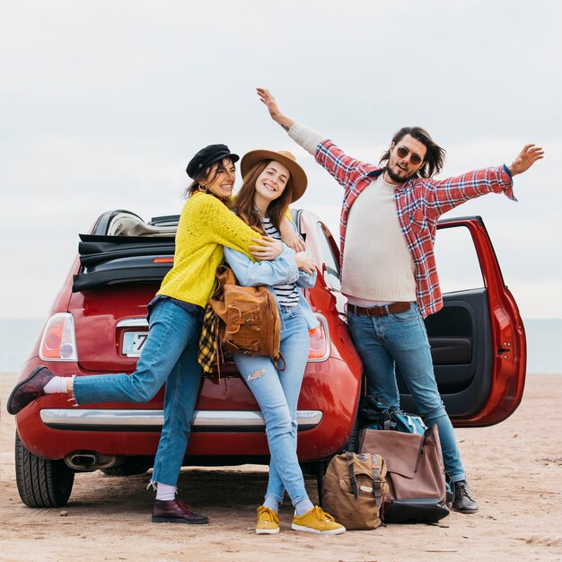 Positive man with upped hands near embracing women and car on beach