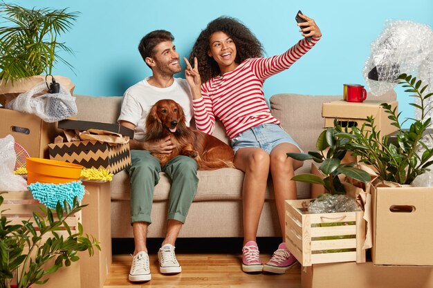 Позитивная супружеская пара на диване с собакой в окружении картонных коробок