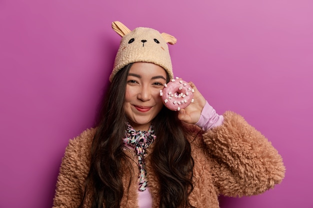 Free photo positive mixed race woman chooses donut for breakfast, decides not to keep diet, poses with favourite dessert