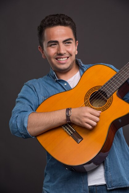 Positive musician playing the guitar on black background