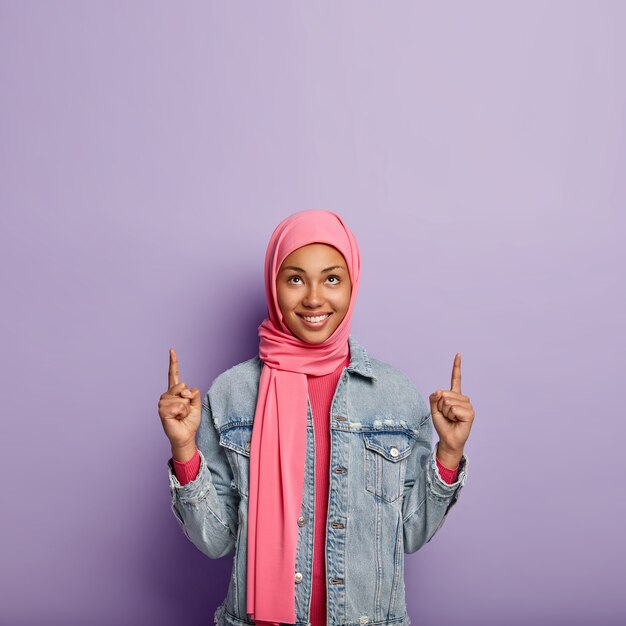 Positive Muslim lady points at top, discusses interesting and happy event happening upwards