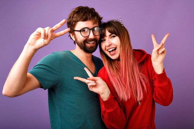 Positive  portrait of crazy young hipster couple having fun together, showing peace gesture laughing and screaming, wearing stylish casual hoodie and T-shirt, family and friends picture