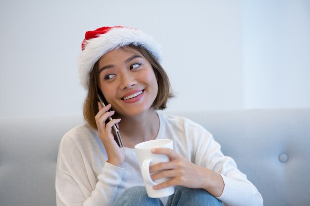 Positive pretty woman in Santa hat talking on mobile phone