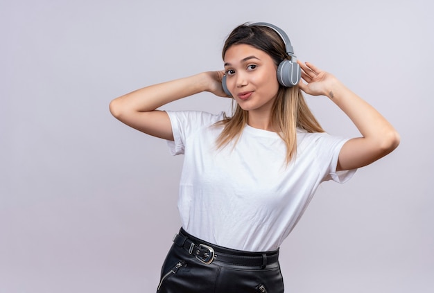 白い壁を見ているヘッドフォンで白いTシャツを着たポジティブなかなり若い女性