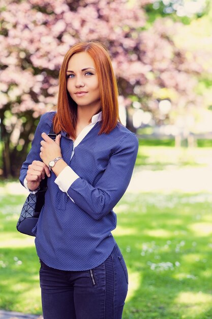 Positive redhead female with backpack posing in a summer park.