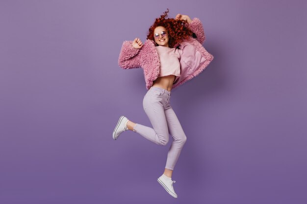 エココート、ピンクのトップと白いズボンのポジティブな赤毛の女の子がライラックのスペースにジャンプします。