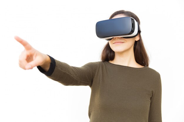 Positive satisfied woman in VR headset pointing finger away